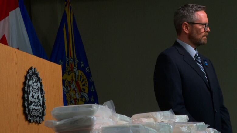 A man stands behind bags of cocaine.