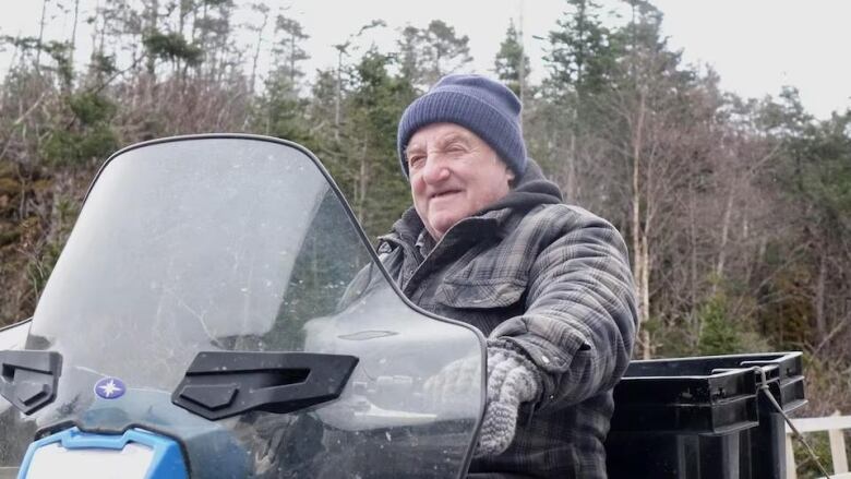 A man in coat and jacket sits behind an ATV.