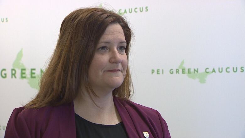 A woman stands in front of a wall with the logo of the P.E.I. Green Party caucus.