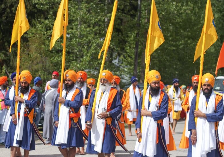 Men with orange turbans are pictured holding orange flags, with many people standing behind them.