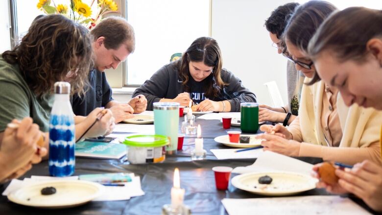 A group of people sit at a table decorating easter eggs.