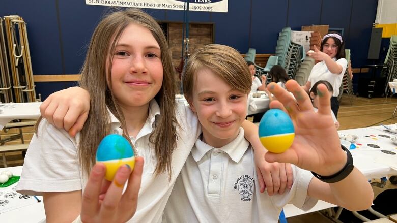 Two students hold up decorated easter eggs.