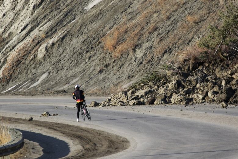 The photo shows a cyclist stopped next to debris from a landslide. 