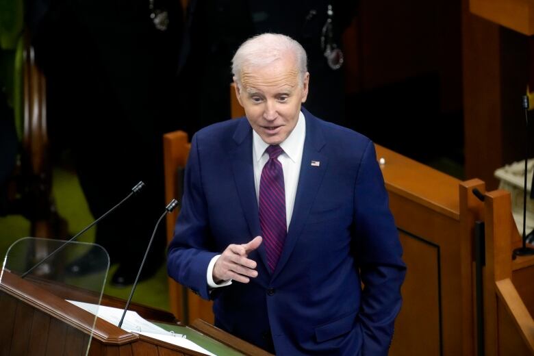 A man in a suit and tie is shown addressing a legislative chamber.