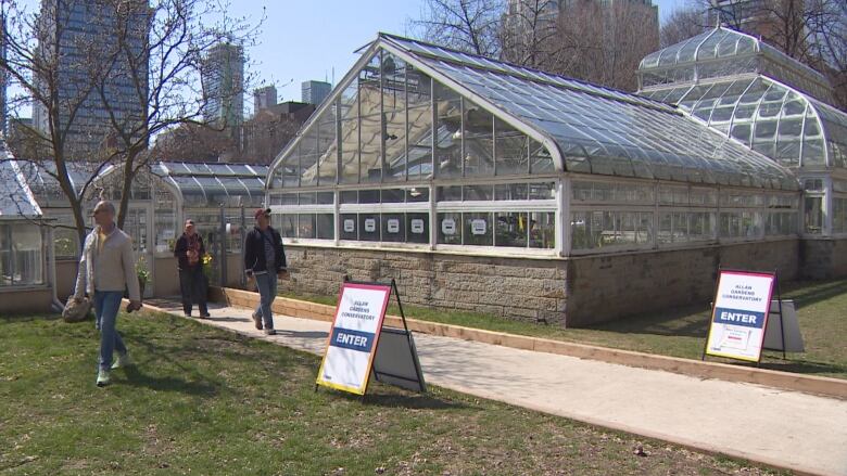 People walk in front of a green house. It's sunny. 