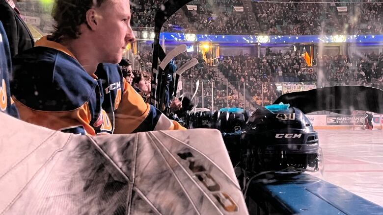 A hockey player sits on the bench with his helmet in front of him