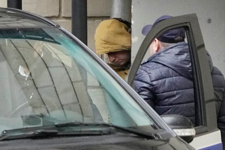 A man wearing a yellow hoodie is escorted into a vehicle by two other men.