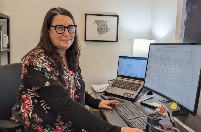 A woman poses at a laptop in an office. 