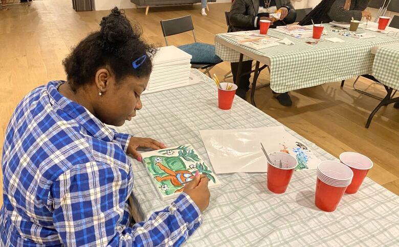 A woman colours at a picnic table indoors. 