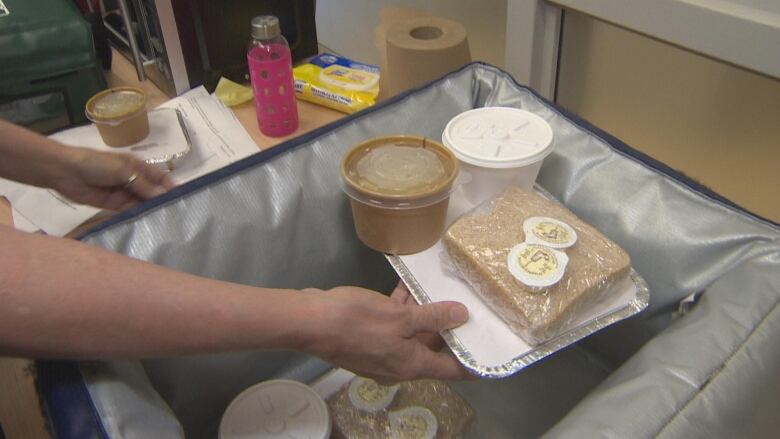 An out-of-frame volunteer places packaged food items into a cooler bag.