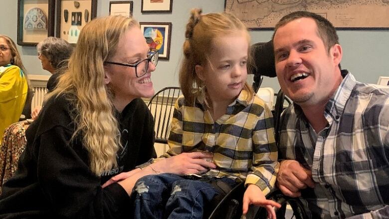 A man and a woman kneel on either side of a child in a wheelchair.