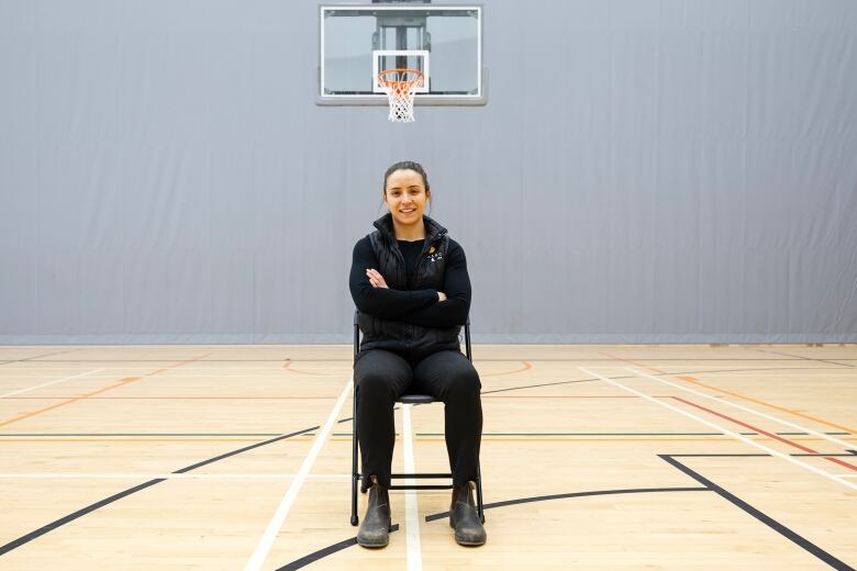 Carriera Lamoureux, Director of Special Projects at MASRC sits on a chair in the middle of a basketball court with her arms crossed and smiles at the camera.