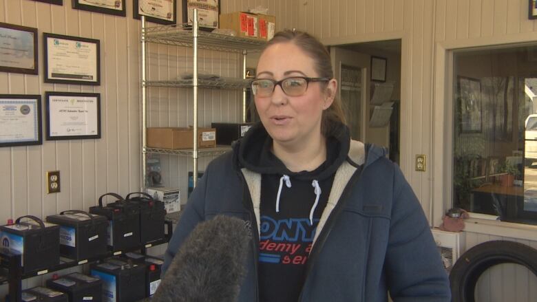 A lady with glasses stands in an autobody shop.