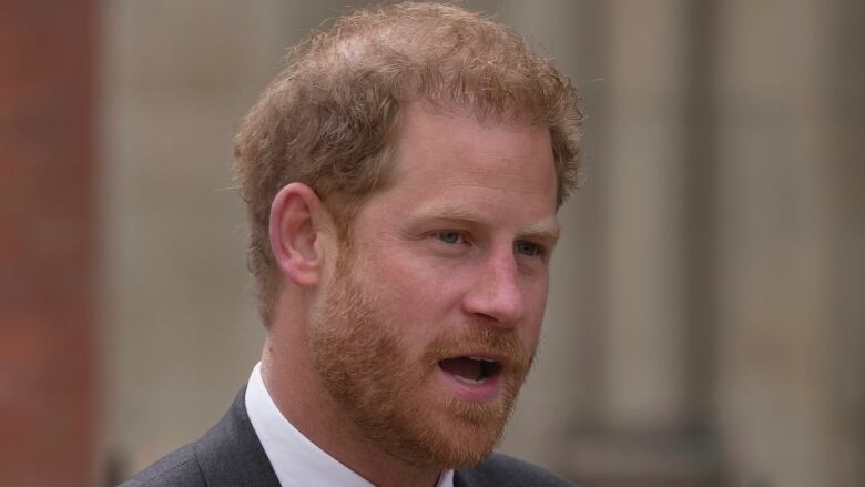 A bearded man wearing a suit is shown closeup.