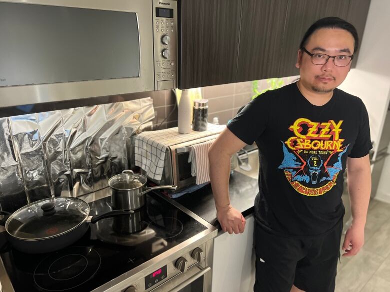 A man is shown in front of his stove in the kitchen of his condo.