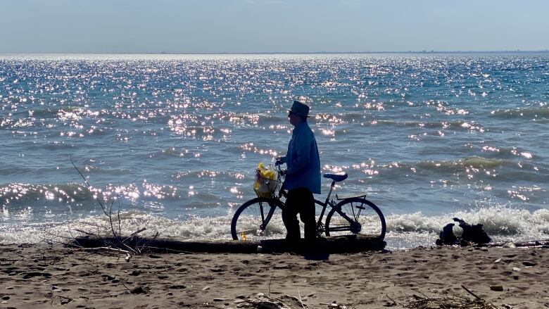 A man on a bike stands on a beach at Toronto Islands 