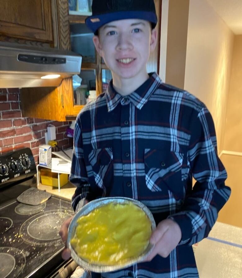 A teenager holds a pie while standing in a kitchen