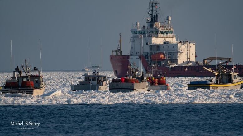 Fishing boats are seen in the foreground surrounded by ice while a Coast Guard ship is seen in the background.