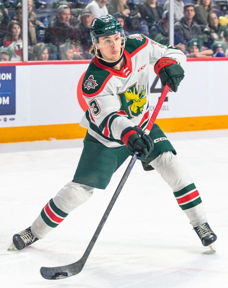 A hockey player in a white, ora0gne and blue jersey shoots the puck.