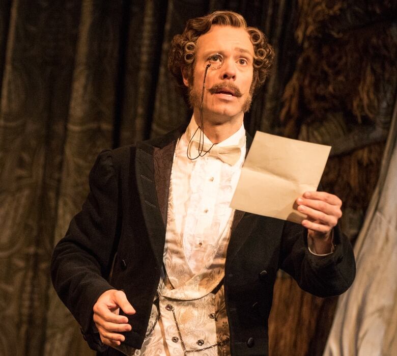 An actor wears a three-piece suit and a monocle while performing in a Broadway show.