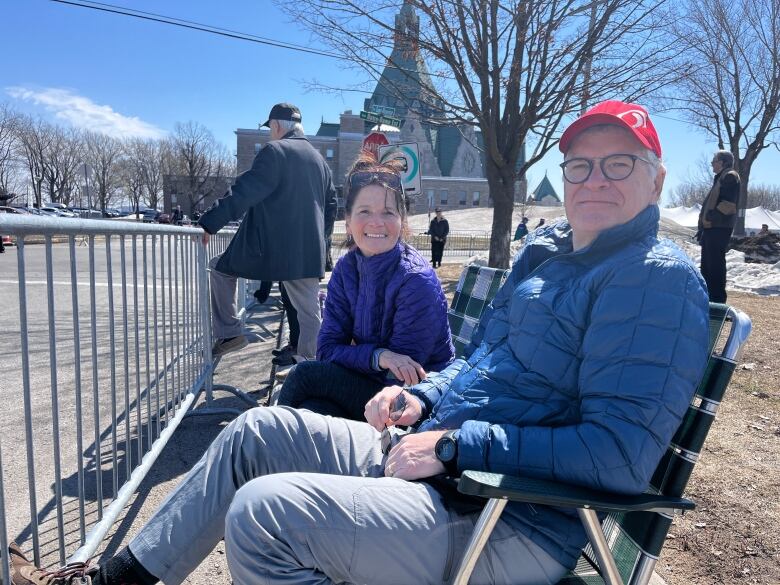 A smiling woman and man in lawn chairs near a church.