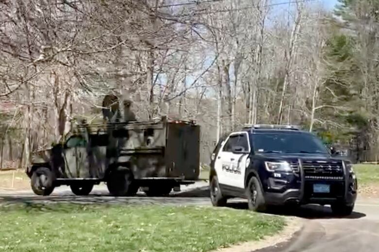 A black and white police vehicle on a driveway with a military-type looking truck.