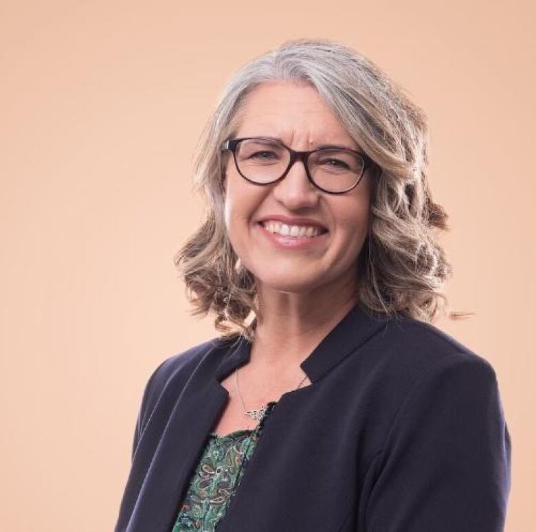 A woman with blonde greying hair and glasses.