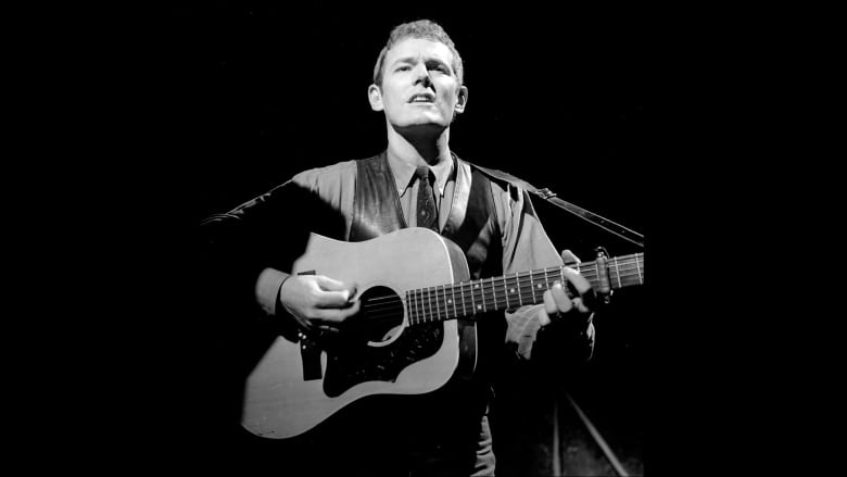 A man sings and plays a guitar on stage.