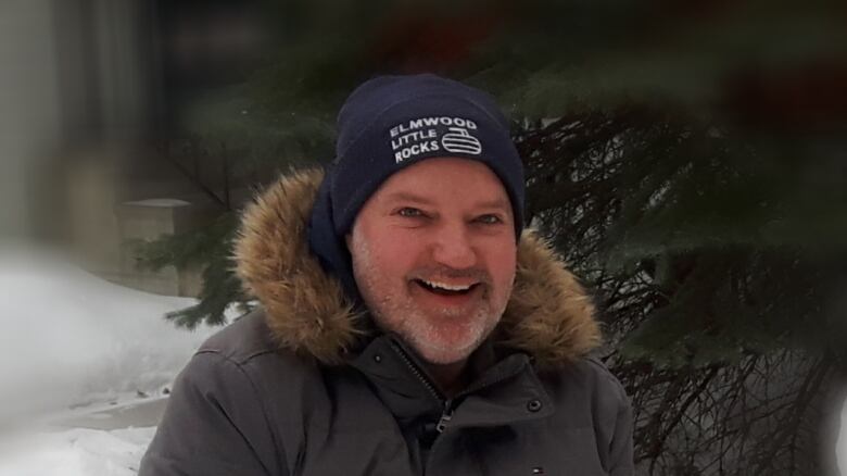 A man in a toque and parka smiles outside in winter.