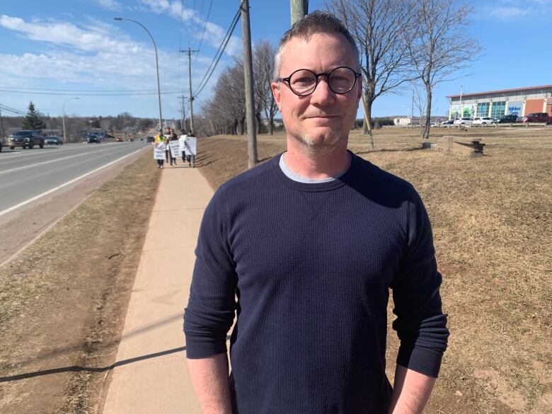 UPEIFA president Michael Arfken stands along on a sidewalk with faculty members marching behind him.