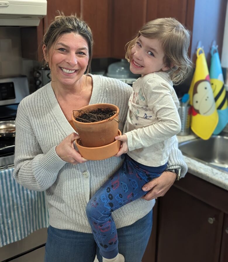 A mother holds her child and a plant pot with a dead plant inside.