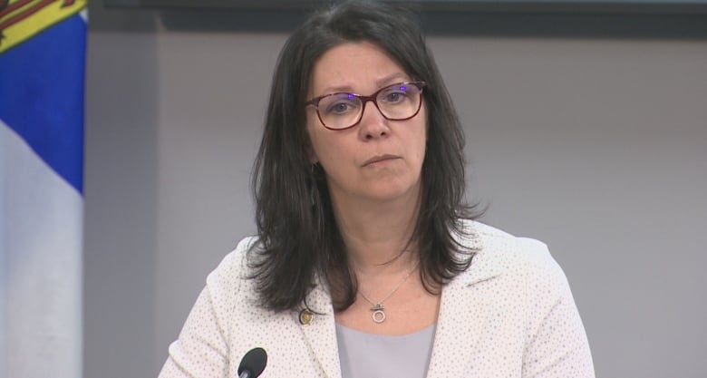 A woman with glasses sits at a podium.