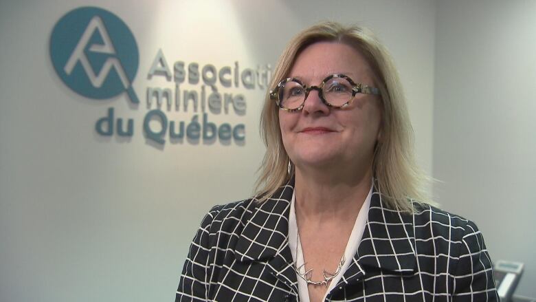 A woman with glasses standing near a sign that says Association minire du Qubec.