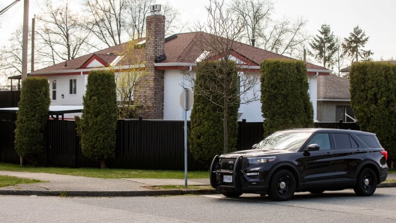 A black SUV is parked in front of a street corner where a house is located behind hedges.