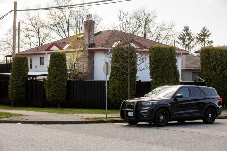 A black SUV is parked in front of a street corner where a house is located behind hedges.