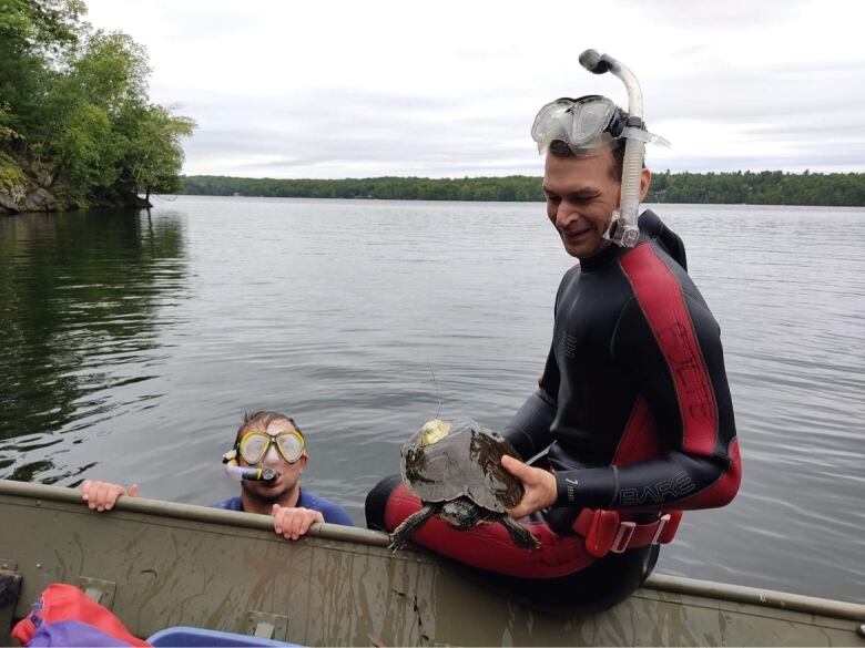 Two people snorkel in a lake. One is holding a turtle.