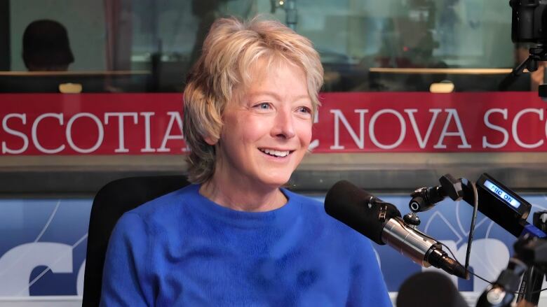 A woman smiles as she sits in front of a microphone in a radio studio.