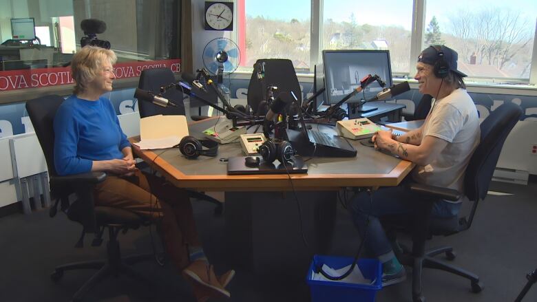 Two people speak across from a table in a radio studio.