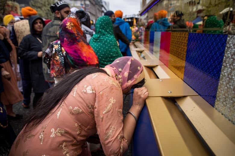 A woman bows down before a parade float, with other people flanking her.