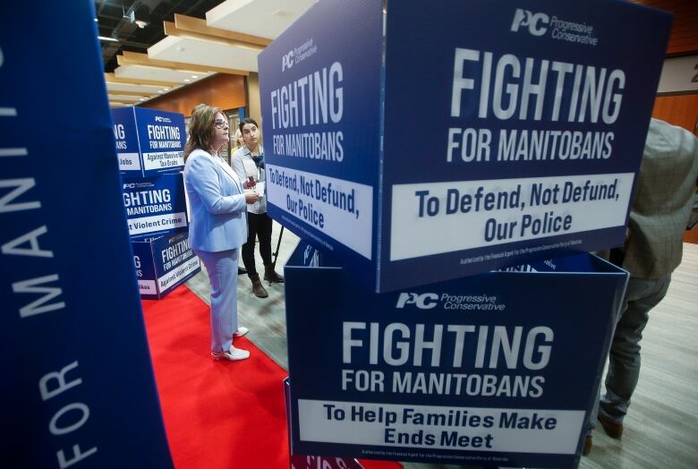 A woman answers questions from the media, on a red carpet and beside signage barring the Progressive Conservatives' new slogan, 'Fighting for Manitobans.'