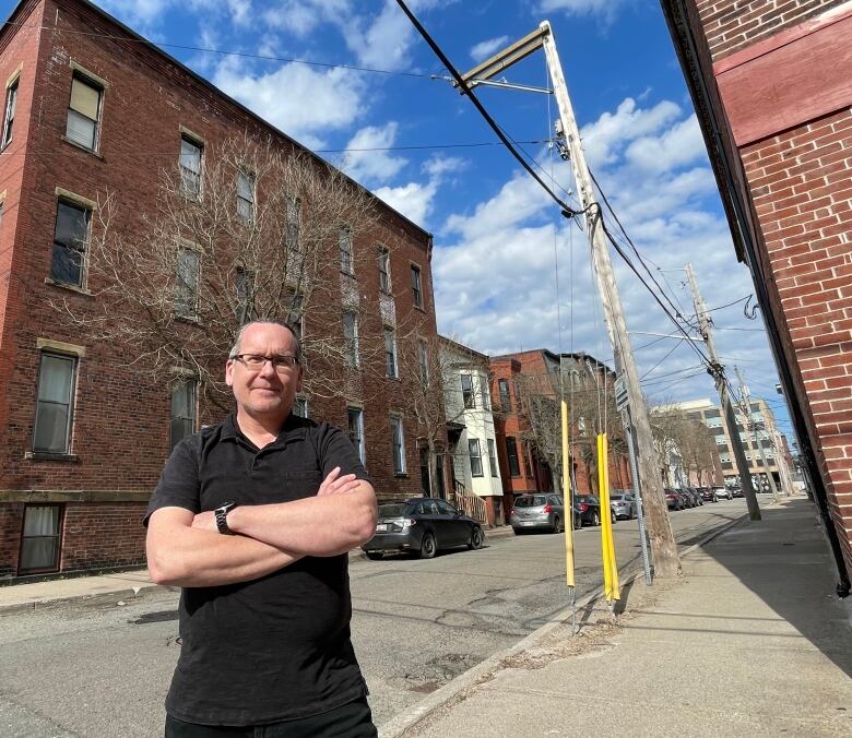 man with arms folded standing in front of large brick apartment building