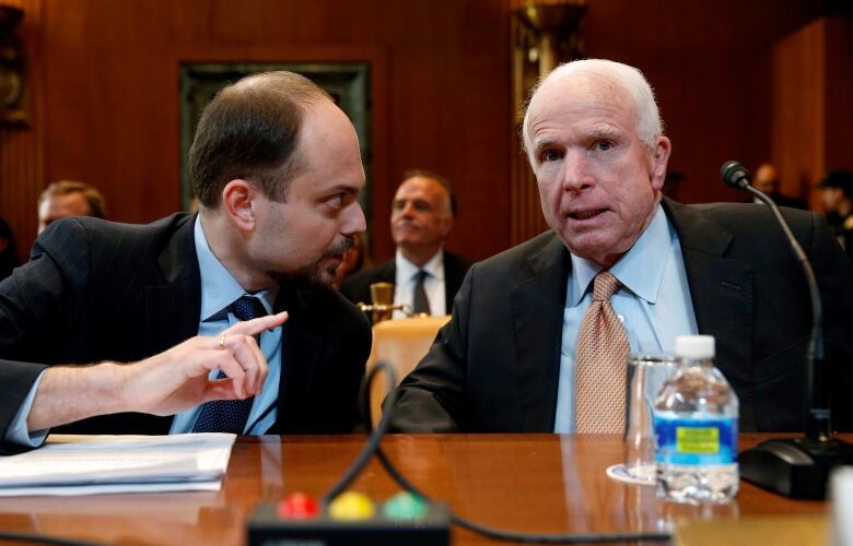 Two men in suits are shown seated inside a room