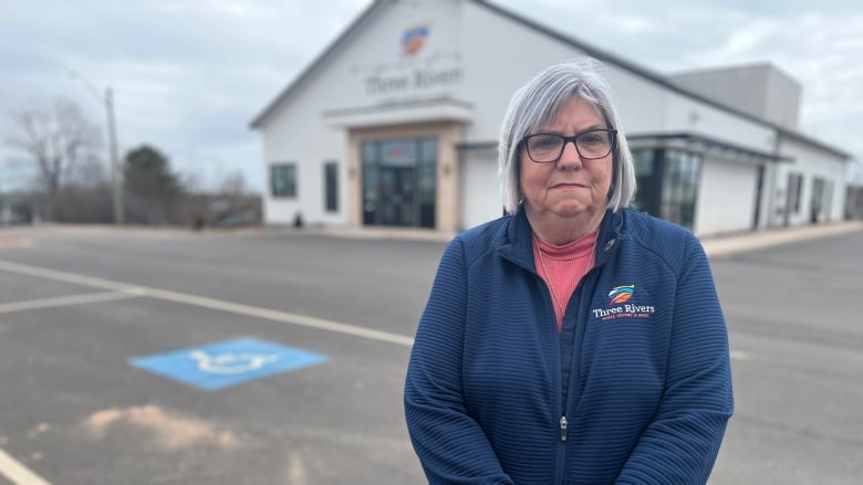 Woman in jacket with Three Rivers logo stands in front of town hall building. 