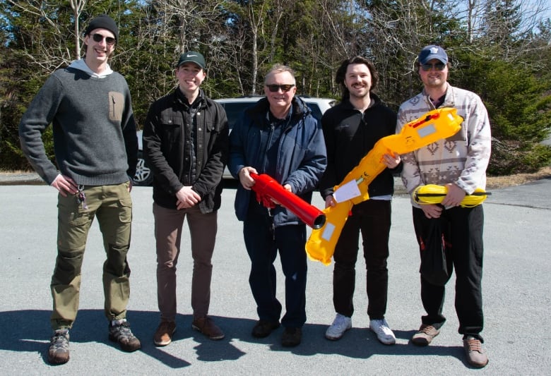 Five men stand together. One man holds a red tube. Another holds a yellow inflatable and a man next to him holds yellow rope.