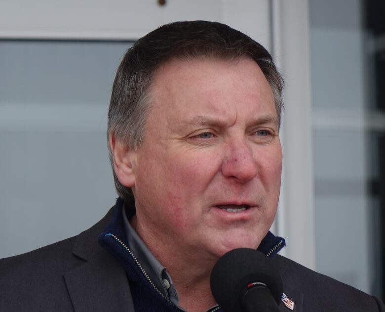 A man with short dark hair speaks into a microphone.