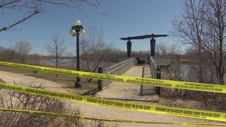 Police tape sections off a gravel path by a river.