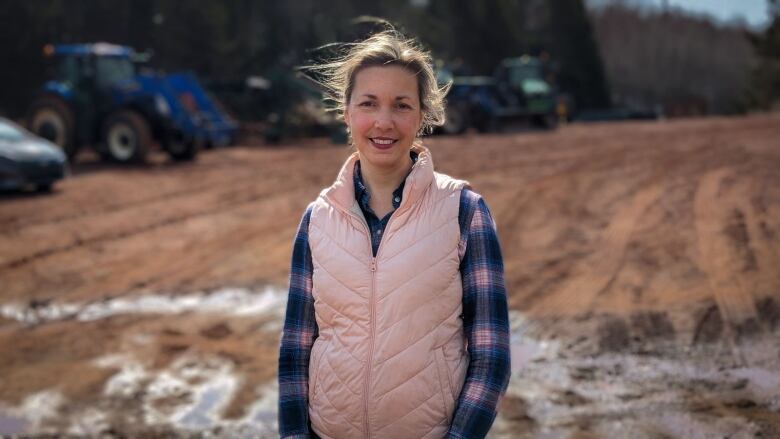 A woman in a pink vest and plaid shirt stands in a farm yard on P.E.I. 