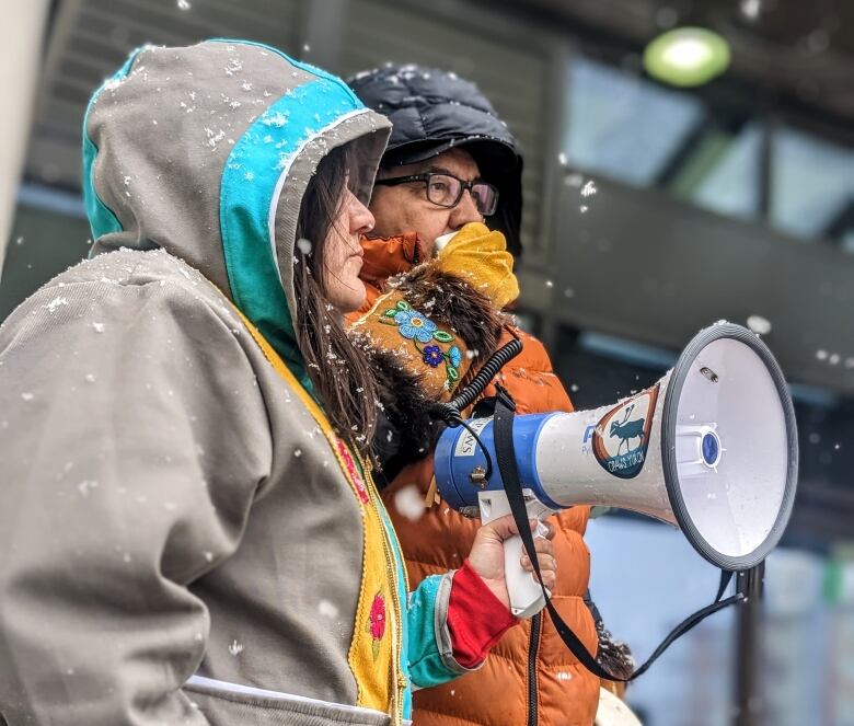 Two people stand on the steps outside a building, with one of them holding a megaphone.