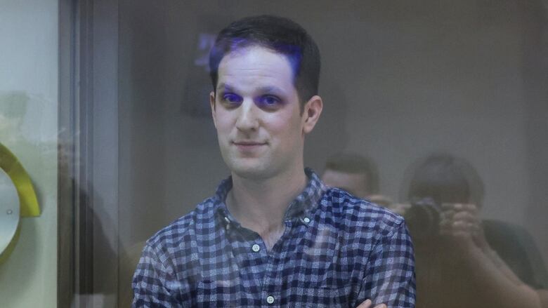 A man in a checkered shirt is seen behind a glass partition.