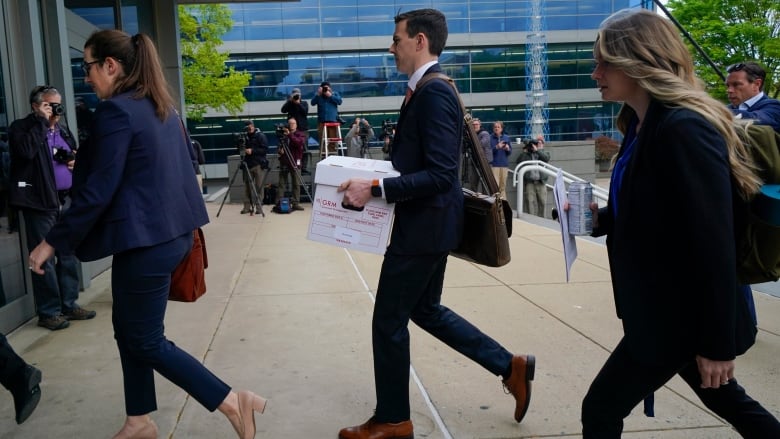 Two women, along with a man carrying a box of documents, enter a court building. 